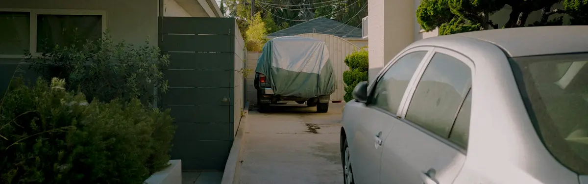 A car parked in a narrow driveway between houses.